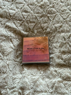 Revolution Glow eyeshdow palett - En snygg eyeshadow palett från Revolution Glow med ett glansigt, fyrkantigt fodral i rosa och guldtoner. Perfekt för att ge huden en fräsch och strålande finish. Paletten har ett tropiskt motiv på locket och är enkel att ta med i väskan.