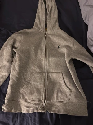 Grå zip hoodie från Polo Ralph Lauren - Snygg grå hoodie med dragkedja från Polo Ralph Lauren. Klassisk design med huva, två stora fickor framtill och den ikoniska lilla loggan broderad på bröstet. Tillverkad i mjukt bomullsmaterial som är perfekt för chill dagar. Pris är definitivt diskuterbart 