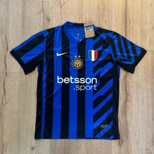 Inter Milan blå-svart matchtröja Nike - Säljer en officiell Inter Milan fotbollströja från Nike i blått och svart med randigt mönster och coola grafiska detaljer. Tröjan har korta ärmar, klubbmärke, sponsortryck och italienska mästarmärket på bröstet. Tillverkad i lätt polyester med Dri-FIT-teknologi.