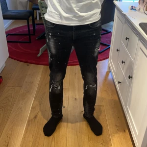 Supply & Demand svarta jeans - Svarta jeans från Supply & Demand med slitna detaljer och vita färgstänk. Jeansen har klassisk femficksdesign, dragkedja och knapp, samt smal passform som sitter tajt längs benen. Materialet är jeans med stretch för extra komfort.