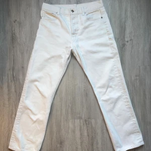 Helmut Lang vita crop straight jeans - Snygga vita jeans från Helmut Lang i modellen Crop Straight. De har klassisk femficksdesign, raka ben och croppad längd. Jeansen är tillverkade i kraftig bomull och har silverfärgade knappar med logga. Perfekta för dig som gillar minimalistisk och clean stil.
