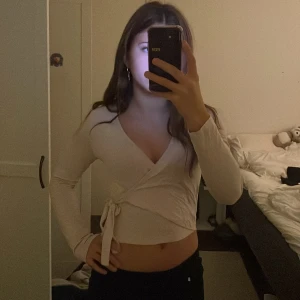 Ljus rosa knyt tröja  - Säljer en beige omlottopp från Gina Tricot med lång ärm och knyt i sidan. Toppen har croppad passform och djup v-ringning