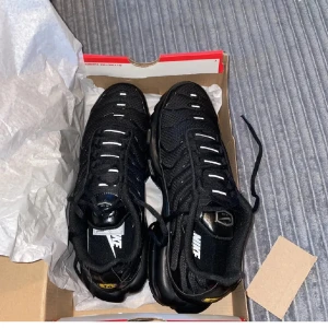 Svarta Nike sneakers Vapormax - Säljer ett par svarta Nike Vapormax sneakers med vit logga och detaljer. Skorna har snörning, platt sula och mesh-överdel för extra ventilation. Snygg och sportig design som passar perfekt för dig som gillar streetwear och vill ha något bekvämt och stilrent.