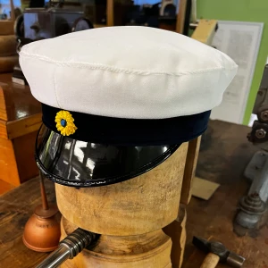 Klassisk Studentmössa 53-63 Uppsala (mörkblå) - Klassisk studentmössa med vit ovandel i bomull, mörkblått band och blank svart skärm. Framtill sitter en klassisk kokard. Insidan har det klassiska foder i blått och gult. Uppsala-modell. Finns storlekar från 52–63. Fråga oss innan beställning (Limiterat lager)