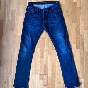 Mörkblå Nudie Jeans Denim 30/32 - Säljer ett par mörkblå jeans från Nudie Jeans, modell Dude Denim. Jeansen har klassisk femficksdesign, kontrastsömmar och är tillverkade av 99% ekologisk bomull och 1% elastan för extra stretch. Stora i storleken.