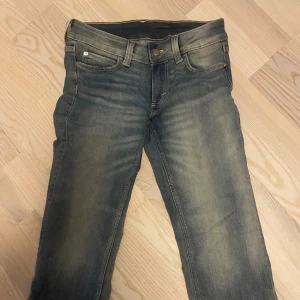 Cheap Monday blå jeans med tryck - Snygga blå jeans från Cheap Monday med coolt vitt tryck och logga på bakfickan. Jeansen har klassisk femficksdesign, raka ben och gul kontrastsöm. Materialet är slitstarkt denim i bomull och passformen är normal. Perfekt för dig som gillar streetstyle.