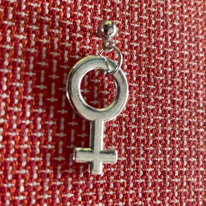 By prisförslag- 1 st Silvrigt örhänge med venus-symbol - Coolt örhänge i silverfärgad metall med venus-symbol. Hängsmycket har en rund cirkel med ett kors nedtill och sitter på en liten kula. Perfekt accessoar för att uttrycka din stil och statement.