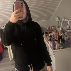 Svart hoodie med rosa tryck - Svart hoodie med huva och snörning, samt långärmad passform. På ryggen finns ett coolt rosa tryck med smileys och hjärtan. Perfekt för dig som gillar streetstyle och vill ha en chill look. Materialet känns mjukt och skönt mot huden.
