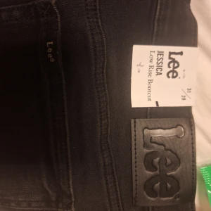 Svarta Lee Jessica bootcut jeans - Säljer ett par svarta Lee Jessica jeans med bootcut-modell och låg midja. Jeansen är i klassisk svart denim med snygga detaljer och Lee-logga på bakfickan. Perfekta för dig som gillar en tidlös och stilren look.