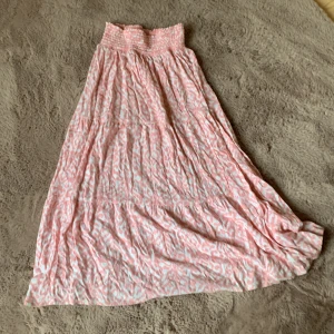 Rosa långklänning med olika mönster  - Säljer en söt och flowy rosa långkjol  med vitt leopardmönster. Kjolen har smock upptill och ett luftigt fall som ger en avslappnad och somrig vibe. Perfekt för dig som gillar mönster och vill sticka ut lite extra!