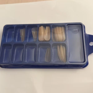 Falska nageltippar i plast - Säljer ett set med transparenta och ljusbeige falska nageltippar i olika storlekar, för dig som vill fixa snygga naglar hemma. Nageltipparna kommer i en blå plastförpackning med flera fack för enkel sortering.
