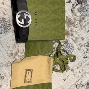 Bälte - Säljer ett svart Gucci bälte i äkta skinn med diskret GG-mönster och ett stort, rundat GG-spänne i silver. Bältet är stilrent och har klassisk form, levereras med originalförpackning och dustbag. Perfekt för dig som vill ha en lyxig accessoar med ikonisk design.