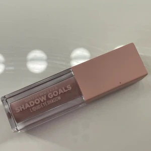 Makeup Mekka Shadow Goals ögonskugga - Flytande ögonskugga från Makeup Mekka i en snygg rosa-nude nyans. Kommer i en stilren rektangulär förpackning med matchande rosa lock och praktisk applikator. Perfekt för att skapa mjuka och trendiga ögonlooks med enkel applicering. Använd 2 gånger så mycket produkt kvar. 
