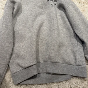 Grå sweatshirt med tryck och stjärna - Grå sweatshirt med svart text 'JE M'EN AMOUR' och en stjärna framtill. Tröjan har ribbade muddar vid ärmslut och nederkant samt lång ärm. Perfekt för en chill och avslappnad stil.