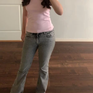 Grå bootcut jeans med låg midja - Snygga grå jeans med bootcut-modell och låg midja. Jeansen har klassisk femficksdesign och dragkedja med knapp framtill. Perfekta för dig som gillar en avslappnad men trendig look.