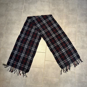 halsduk från Burberry - Snygg halsduk från Burberry 100% lammull. Fint skick förutom att den har en brännskada (bild 2,3). Längden är 170cm (ej fransar inräknat). Hör av er vid frågor eller funderingar!🤩✌️