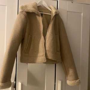 Beige teddyjacka med dragkedja - Snygg beige teddyjacka med mjukt foder och krage i teddy. Jackan har croppad passform, långa ärmar och dragkedja framtill. Perfekt för kyliga dagar och ger en trendig look.PRIS KAN DISKUTERAS 
