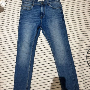 Blå skinny jeans från Pull&Bear - Snygga blå jeans från Pull&Bear i klassisk skinny fit. Jeansen har fem fickor, bälteshällor och dragkedjegylf. Materialet är mjukt denim i bomull med en lätt tvättad look. Perfekta för en trendig och avslappnad stil.