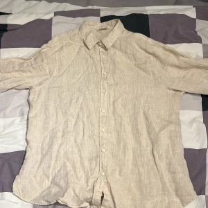 Beige linneskjorta från Stories S - Snygg beige skjorta i linne från Stories, storlek S (36-38). Skjortan har klassisk krage, knäppning framtill och långa ärmar. Perfekt för en chill och stilren look under varmare dagar.