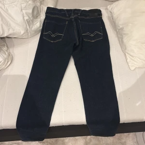 Replay Anbass mörkblå jeans, stl W29 L30 - Snygga Replay Anbass jeans i mörkblå färg. Jeansen har raka ben och normal passform, med Replay-logga på fickan och coola detaljer på bakfickorna. Perfekt för dig som gillar stilrena och tidlösa jeans. Köpte de nyligen men tyckte inte att dem passade så inprincip aldrig använda. W29 L30