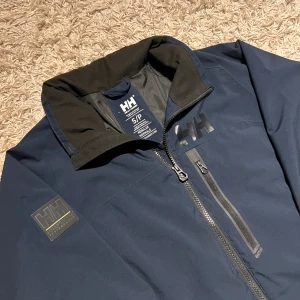 Helly hansen vindjacka mörkblå S herr  - Mörkblå vindjacka från Helly Hansen i storlek S. Mycket bra skick, nästan ny utan defekter. Fickor med kedja och justerbar midja. Postas samma dag slm köp eller dagen därpå🙌💯
