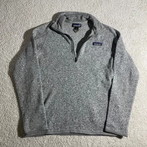 Grå fleece half zip från Patagonia | M/S - Mysig gråmelerad fleece från Patagonia i storlek M. Tröjan har half zip framtill, lång ärm och en praktisk ficka med dragkedja på ena ärmen. Perfekt för kyliga dagar och outdoor vibes.