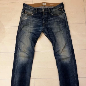 Replay jeans blå straight fit - Ett par riktigt feta Replay  jeans i blå tvätt med slitningar och schyssta fades. Modellen har rak passform och normal midja, med Replay-logga på bakfickan och detaljerade sömmar. Perfekta för att ha till skolan, jobbet eller en biokväll!🙌 Har lagningar i skrevet då det gått sönder lite. Storlek W33 L34 men har sytts upp till L33