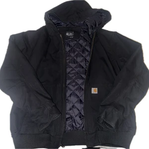Svart Carhartt jacka Loose Fit L - Svart hoodiejacka från Carhartt i loose fit, storlek L. Jackan har quiltat foder, dragkedja framtill, huva och ribbade muddar. Skick: Helt ny, använd 2-3 gånger.