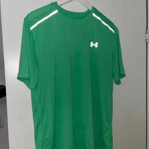 Grön Under Armour Tech T-shirt - Grön Under Armour T-shirt i loose fit med korta ärmar. Tillverkad i lätt och snabbtorkande polyester, perfekt för träning. Reflekterande detaljer på axlarna och klassisk logga framtill och bak i vitt. Snygg och sportig basic för dig som gillar att röra på dig. Storlek M, säljs då jag växt ur den.