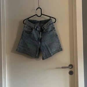 Blå denimshorts från Bik Bok - Snygga blå denimshorts från Bik Bok i klassisk femficksmodell med hög midja och uppvikta benslut. Lite längre shorts i storlek 38.  