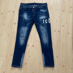DSQUARED2 blå slim jeans med tryck - Snygga blå jeans från DSQUARED2 i slim fit med coolt 'ICON' tryck och slitna detaljer. Jeansen har klassisk femficksdesign, kontrastsömmar och en mörk tvätt med ljusa partier. Materialet är jeans och passformen är tight, perfekt för dig som gillar streetstyle. Använt 2 gånger så helt nya.Priset kan diskuteras👍