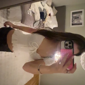 Vit croppad blus med volang och knyt - Säljer en söt vit croppad blus med volangkant och knyt framtill. Toppen har korta ärmar och en smickrande v-ringning. Perfekt för dig som gillar romantisk och trendig stil. Materialet känns lätt och luftigt.