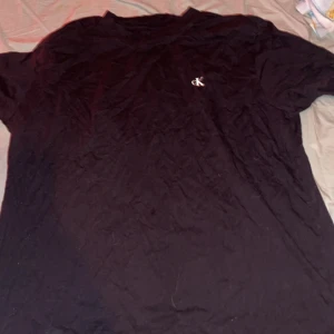 Svart Calvin Klein Jeans t-shirt XXL - Svart t-shirt från Calvin Klein Jeans i storlek XXL. Framsidan har en liten CK-logga på bröstet och baksidan har ett stort, vitt tryck med CALVIN KLEIN JEANS. Klassisk rund hals och korta ärmar. Mjuk bomullskvalitet som är skön mot huden.