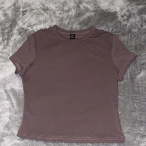 Brun kortärmad topp från SHEIN - En basic brun topp från SHEIN i storlek M. Modellen är figurnära med korta ärmar och rund halsringning, även lite kort i modellen. T-shirten är enkel och stilren, perfekt att matcha med jeans eller kjol. Materialet känns mjukt och stretchigt. 