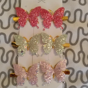 Glittriga fjärilsdiadem - Säljer ett set med sex diadem i form av fjärilar, täckta med glitter i rosa, ljusgrön och ljusrosa. Fjärilarna har guldfärgade detaljer och sitter på hårklämmor. Perfekt för att ge din frisyr extra bling och färg. Superfina till alla som gillar glitter och söta accessoarer.