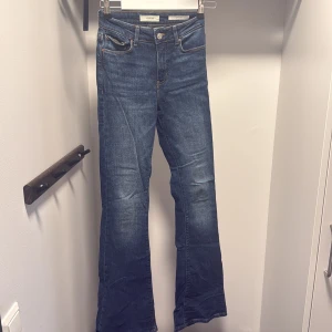 Blåa flare jeans från Guess - Snygga blåa jeans från Guess i modellen Sexy Flare. Jeansen har klassisk femficksdesign, orange kontrastsömmar och ett ikoniskt rött Guess-märke på bakfickan. Modellen har utsvängda ben och är tillverkad i ett mjukt denimtyg med skön passform.