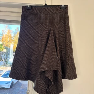 Brun rutig asymmetrisk kjol från Mexx - Snygg brun rutig kjol från Mexx med asymmetrisk nederkant och bred linning. Kjolen har dragkedja bak och är fodrad för extra komfort. Perfekt för dig som gillar en unik och trendig stil med klassiska vibbar.