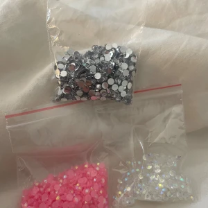 Strass-stenar för smink i tre färger - Tre påsar med strass-stenar för ansikts- och ögonsmink. En påse med silvriga stenar, en med rosa och en med iriserande vita. Perfekta för kreativa sminkningar och festivallooks. Stenarna är runda och platta undertill för enkel applicering med lim.