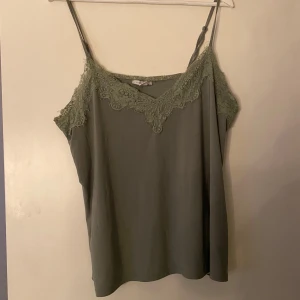 Grön linnetopp med spets från Amisu - Snygg ljusgrön linnetopp från Amisu med tunna axelband och v-ringning dekorerad med spetsdetaljer. Toppen är ärmlös och har en mjuk, flowy passform som känns lätt och luftig. Perfekt för varma dagar eller lager på lager.💚Frakt ingår inte 