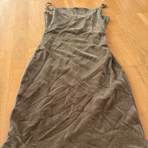 Glittrig brun klänning från BikBok - Supersnygg glittrig brun klänning från BikBok med smala axelband. Klänningen är figurnära och har en kort längd, perfekt för dig som vill sticka ut. Materialet är mjukt och skimrar snyggt i ljuset. Enkel men ändå extra med sitt glittriga tyg. Perfekt för nyår eller ett annat firande!