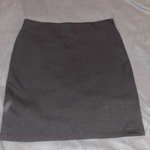 Svart tight kortkjol från H&M - Enkel och stilren svart kortkjol från H&M i tight passform. Kjolen är rak i modellen och tillverkad i mjuk bomullsblandning med stretch, perfekt att matcha med en crop top eller oversized hoodie.