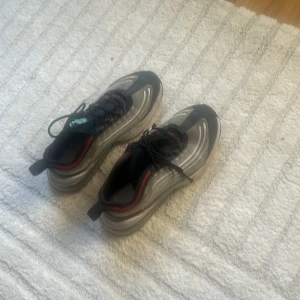 Nike sneakers i silver och svart - Nike sneakers med futuristisk design i silver och svart med röda detaljer. Skorna har snörning, rund tå och en unik sula med röda och transparenta partier. Ovandelen är i syntetmaterial och mesh för bra andningsförmåga. Perfekta för dig som gillar sportig och modern stil.