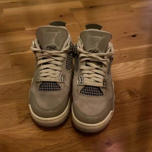 Nike Air Jordan 4 x A Ma Maniére grå - Säljer ett par Nike Air Jordan 4 x A Ma Maniére i grått och vitt. Skorna har meshpaneler, mockadetaljer och klassisk Jumpman-logga på häl och plös. Snygga detaljer i silver och broderad text på insidan. Perfekta för dig som gillar unika sneakers.