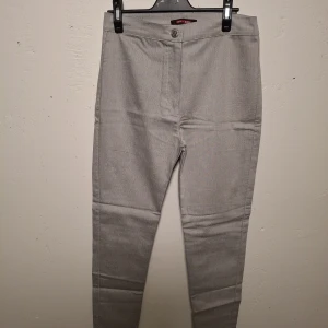 Gråa slim byxa  Storlek 38-40  - Snygga grå kostymbyxor från Eckö Unltd med slim passform. Byxorna har klassisk design med två bakfickor och stängs med knapp och dragkedja. Perfekta för en clean och stilren look.