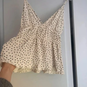 Prickig vit linnetopp med volang - Supersöt vit linnetopp med svarta prickar och tunna axelband. Toppen har v-ringning