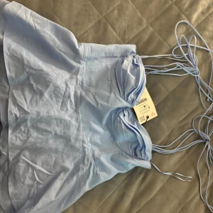 Ljusblå korsett-topp med snörning - Supersöt ljusblå korsett-topp från ZARA med tunna axelband och snygg snörning. Toppen har formade kupor och smock i ryggen för extra komfort. Perfekt för att skapa en trendig look i sommar!