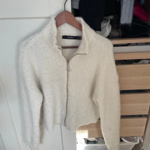 Vit stickad kofta med dragkedja - Mysig vit stickad kofta från Vero Moda med dragkedja framtill och hög krage. Perfekt för lager-på-lager och chill dagar. Långärmad och ribbad vid ärmslut och nederkant. Enkel att matcha med jeans eller kjol.