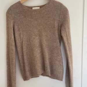 Beige stickad tröja med rund hals - Mysig beige stickad tröja med rund halsringning och långa ärmar. Perfekt för lager-på-lager och passar till allt. Tröjan har en enkel och stilren design med ribbade muddar vid ärmslut och nederkant.