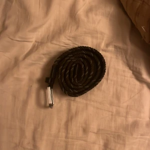 Svart flätat bälte från Onewear - Snyggt svart flätat bälte från Onewear Sweden med silvrigt spänne. Bältet är gjort i syntetmaterial och har en stilren look som passar till jeans eller chinos. Flätad design gör det enkelt att justera längden efter behov.