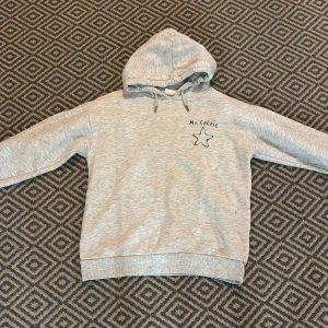 Grå hoodie med stjärntryck Ma Cherie - Grå hoodie med huva och snörning, tryck med texten 'Ma Cherie' och en stjärna både fram och bak. Mjuk och skön, perfekt för chill dagar. Ribbade muddar vid ärmslut och nederkant. Oversized fit för en avslappnad look.